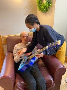 Client holds guitar while staff assists